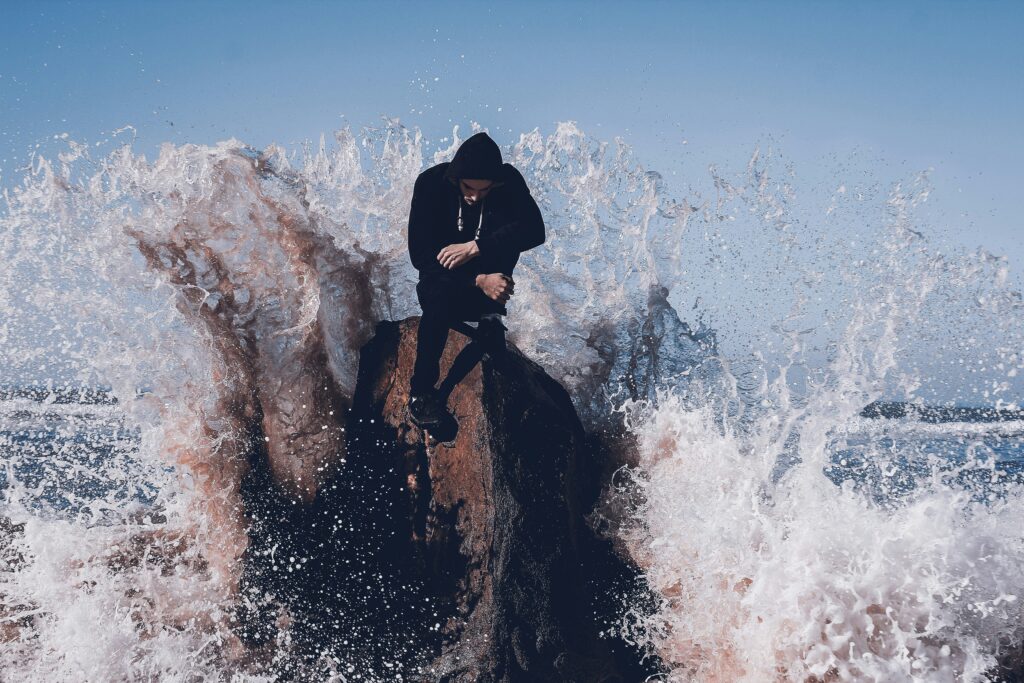 a man sitting on a rock with waves splashing around him