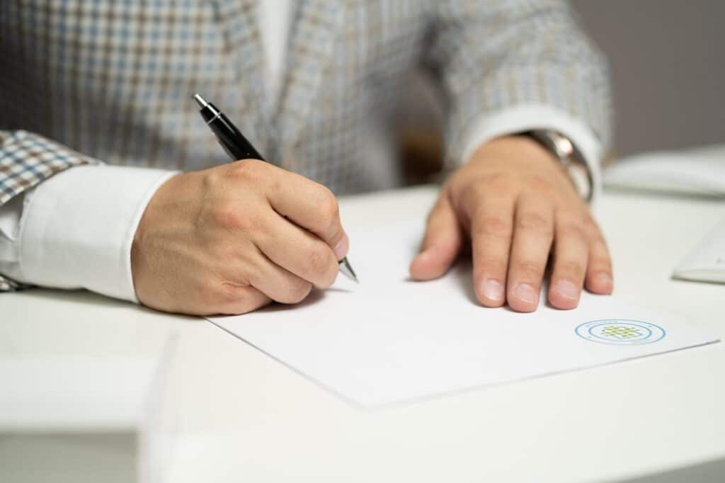 Man in grey suit signing contract which may contain a force majeure clause EM Law