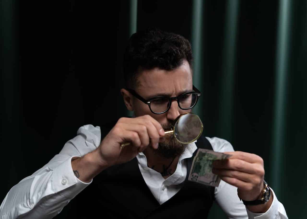 Man with magnifying glass examining money in EM Law blog on Joint Ventures
