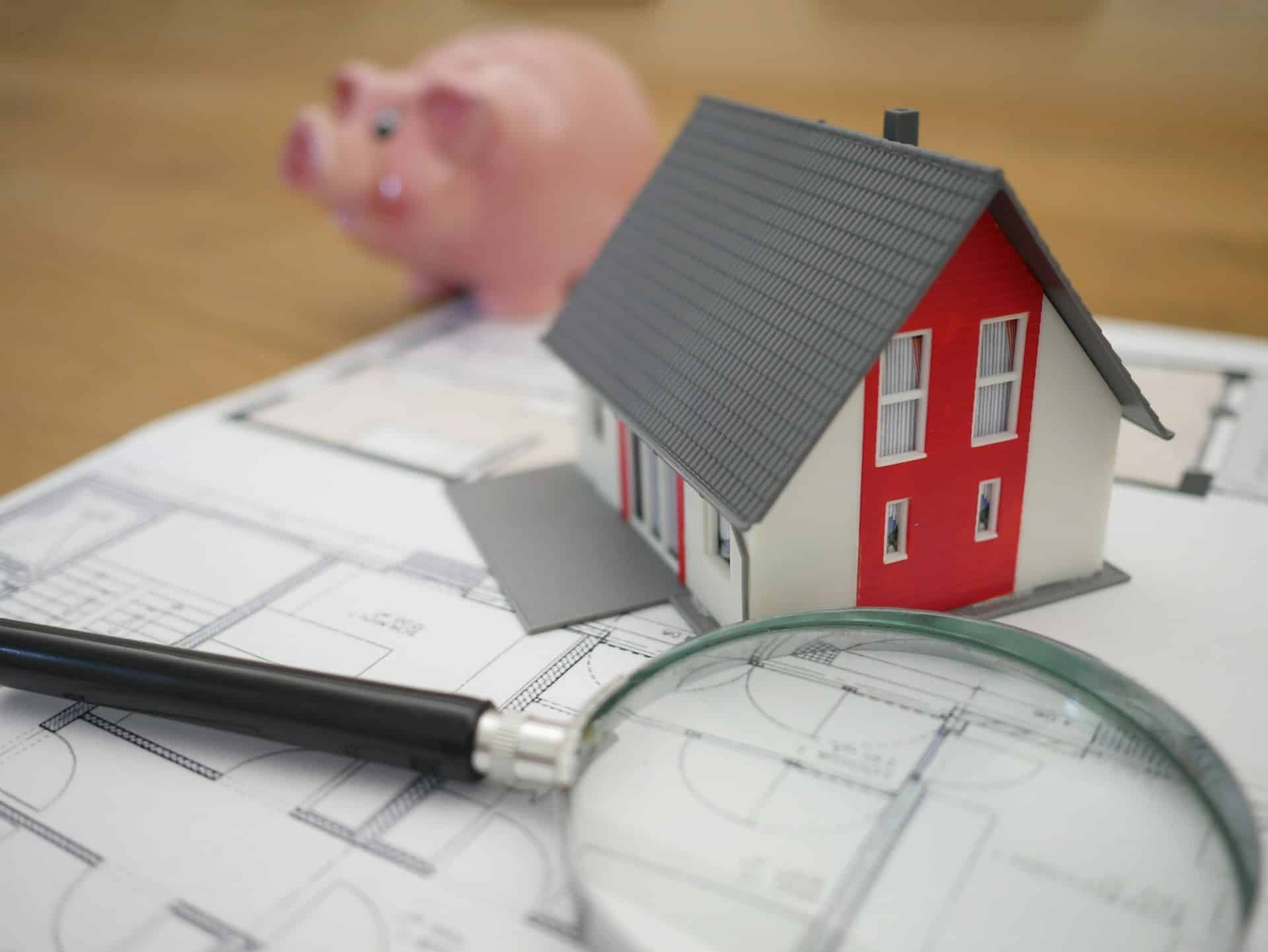 Small fake house on a floor plan next to a piggy bank in a EM Law blog on forfeiture of a commercial lease